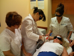 Two students observe a National Laser Institute teacher performing a hair removal procedure on a live patient.